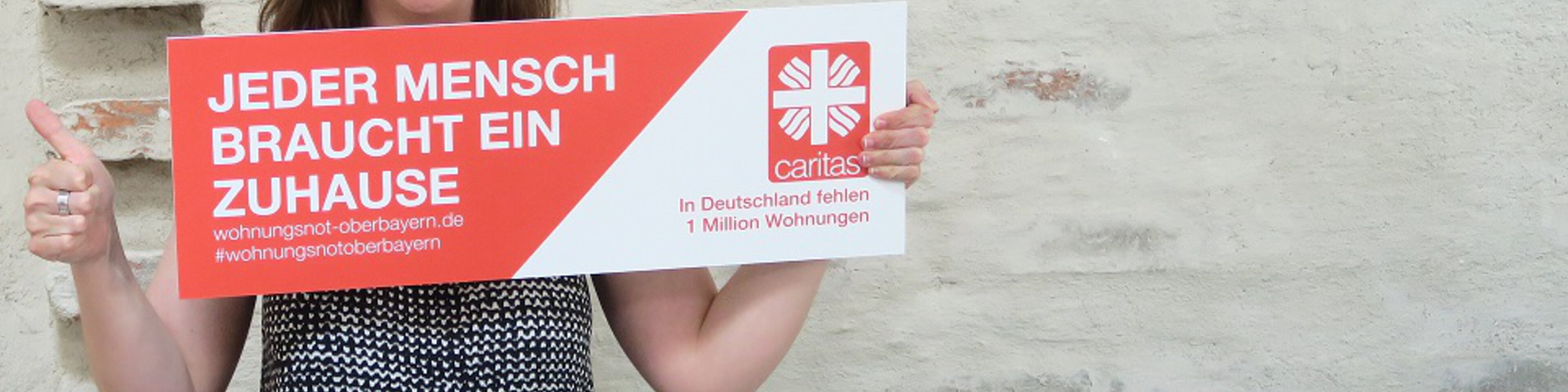 Frau hält "Jeder Mensch braucht ein Zuhause"-Schild | © Caritas München Oberbayern