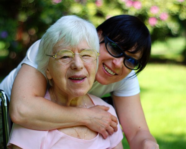 Frau umarmt ältere Dame im Rollstuhl von hinten | © Kempski - iStock