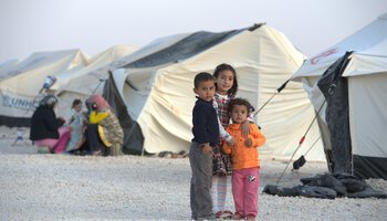 Drei kleine Migranten-Kinder stehen neben Zelten | © Paul Jeffrey