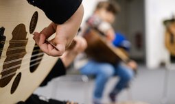 Eine Kinderhand zupft an Gitarrenseiten | © Superar | Caritas München und Oberbayern