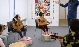 Ein Gruppe mit Kinder sitzt zusammen und lernen Gitarre spielen | © Superar | Caritas München und Oberbayern